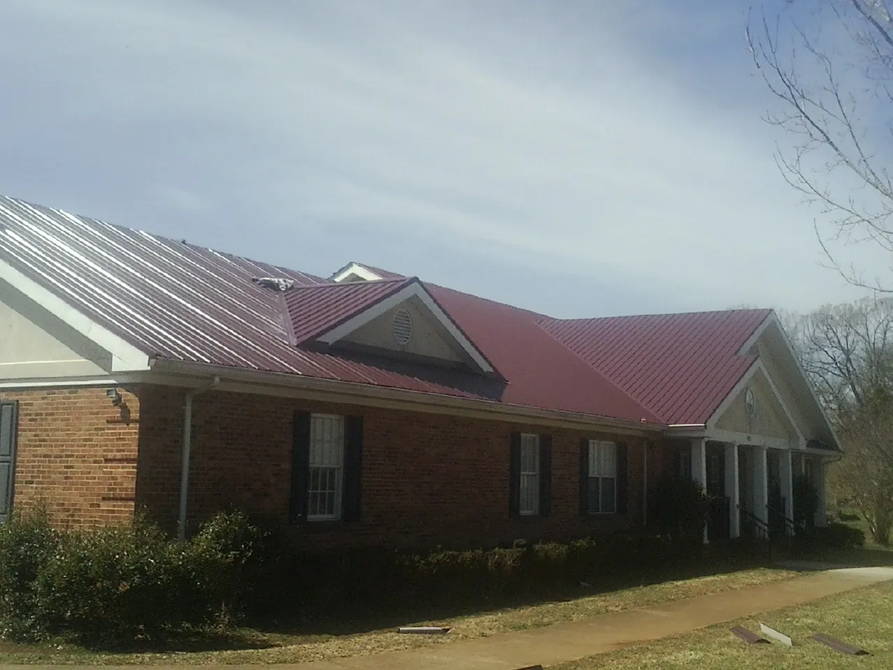 Red metal roof with gabled entries on a long brick building, from a Hail Damage Roof Repair job in Thorofare