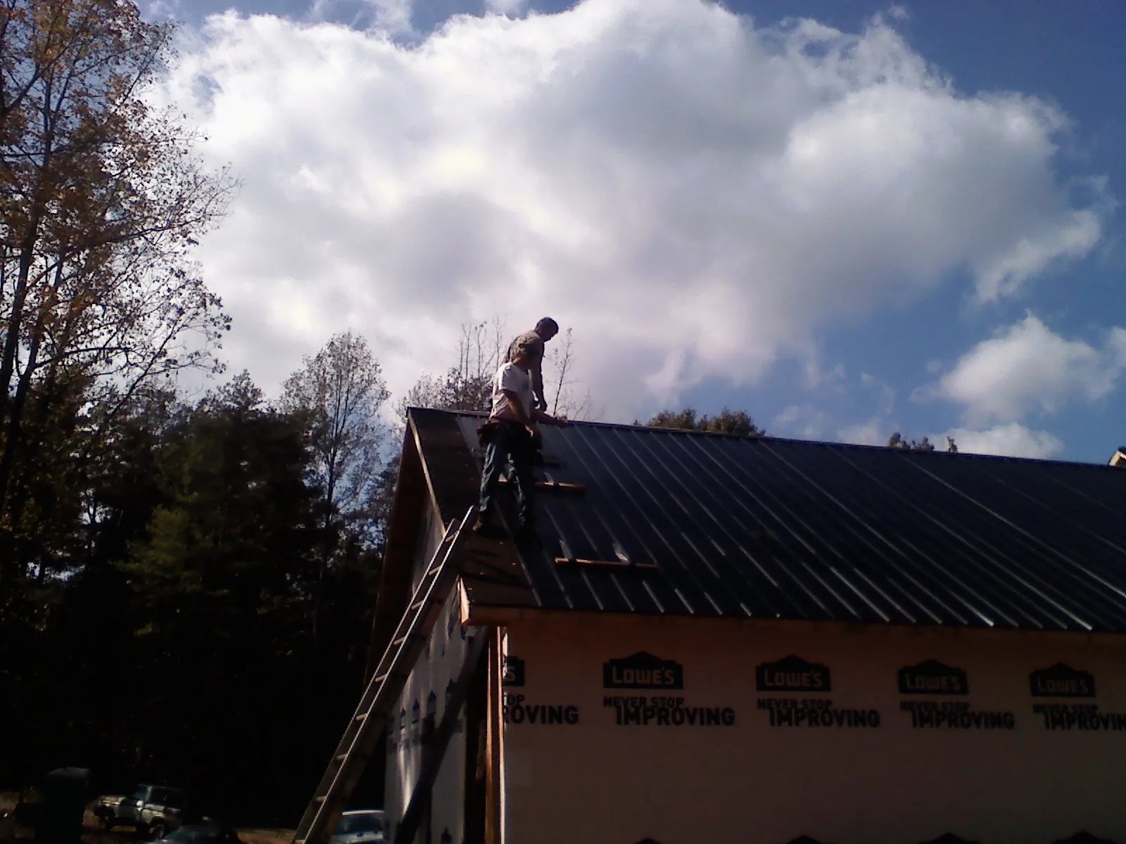Roofer fastening dark metal panels high against a cloudy sky, from a Roof Inspection job in Thorofare