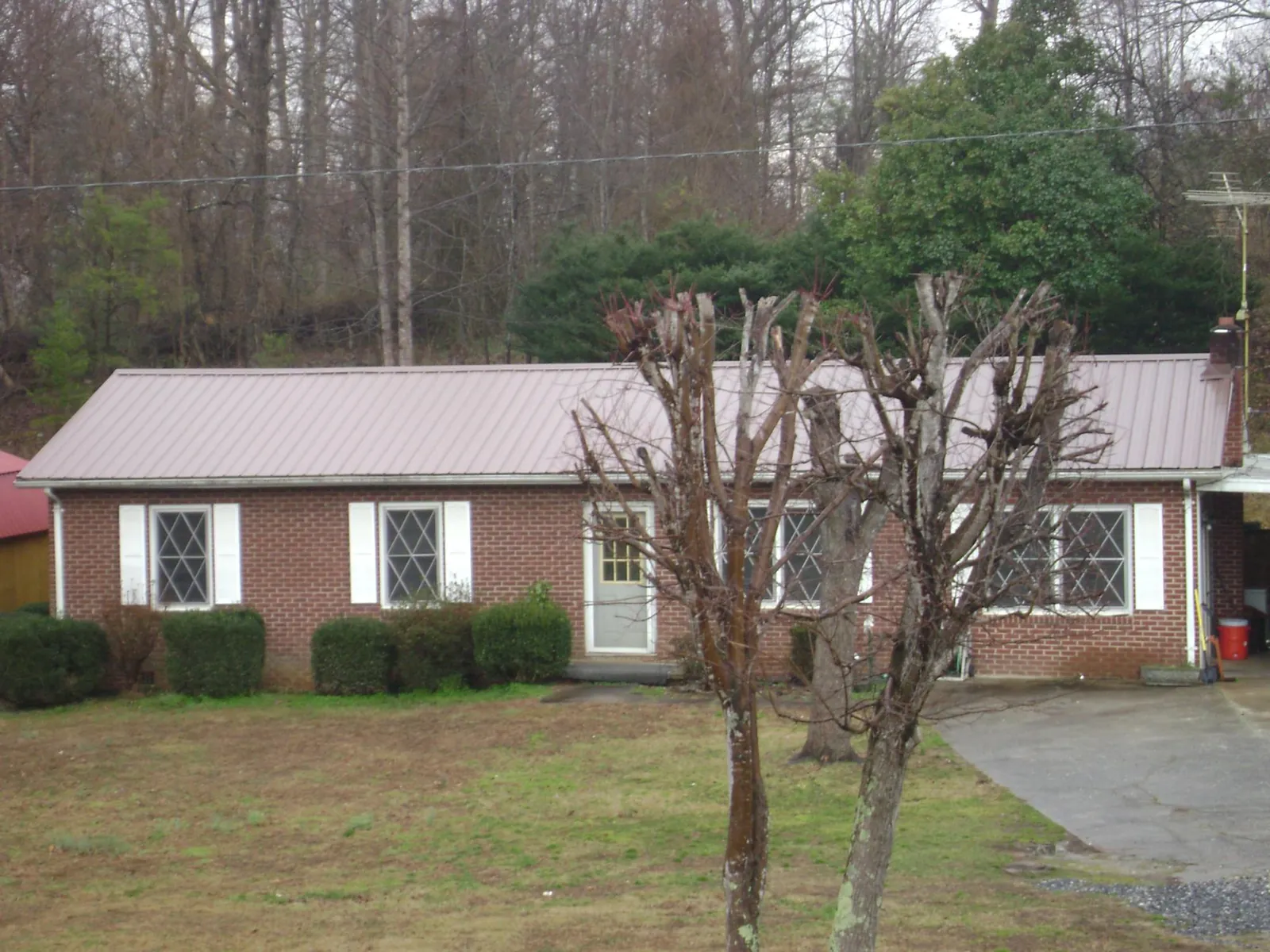 Mauve metal roof on a brick ranch home behind bare trees in Thorofare