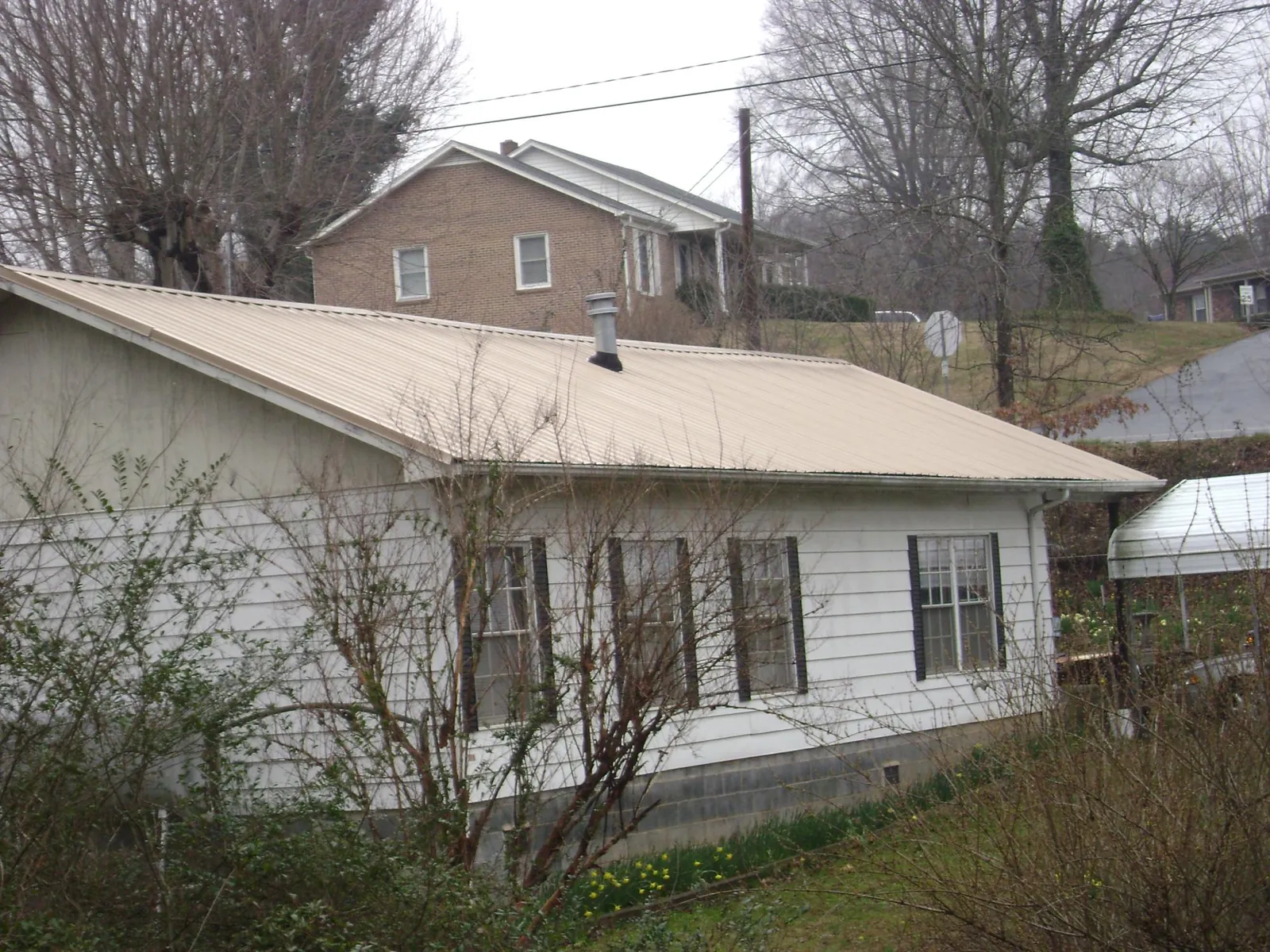 Tan metal roof on a white sided house set into a hillside — Commercial Roofing by Roofing Brothers in Thorofare